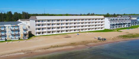 Un hôtel à plusieurs étages doté de balcons, d’une plage avec des chaises longues et offrant une vue sur l’eau.