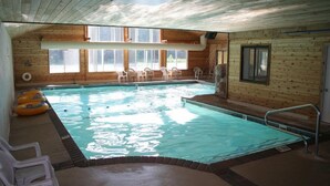 An indoor swimming pool with clear water, surrounded by wooden walls and large windows.