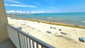 A beach view from a balcony with a railing, sandy beach, and ocean.
