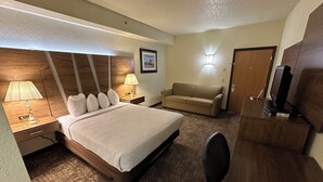 A hotel room with a bed, a desk with a computer, a sofa, and a television.