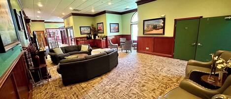 A spacious lobby with a patterned carpet, a large sectional sofa, a leather armchair, and a green cabinet.
