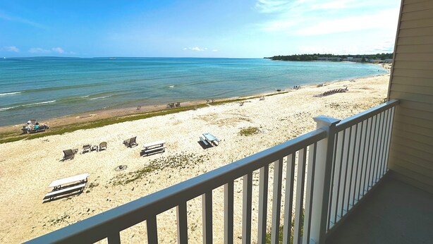 A beach view from a balcony with a railing, sandy beach, and ocean.