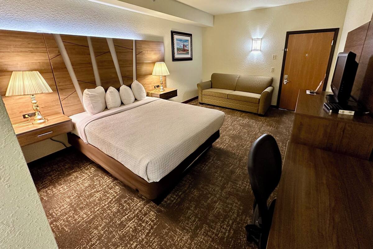 Ein Hotelzimmer mit einem großen Bett, einem Schreibtisch, einem Sessel, einer Couch, einem Fernseher und einem Bild an der Wand.