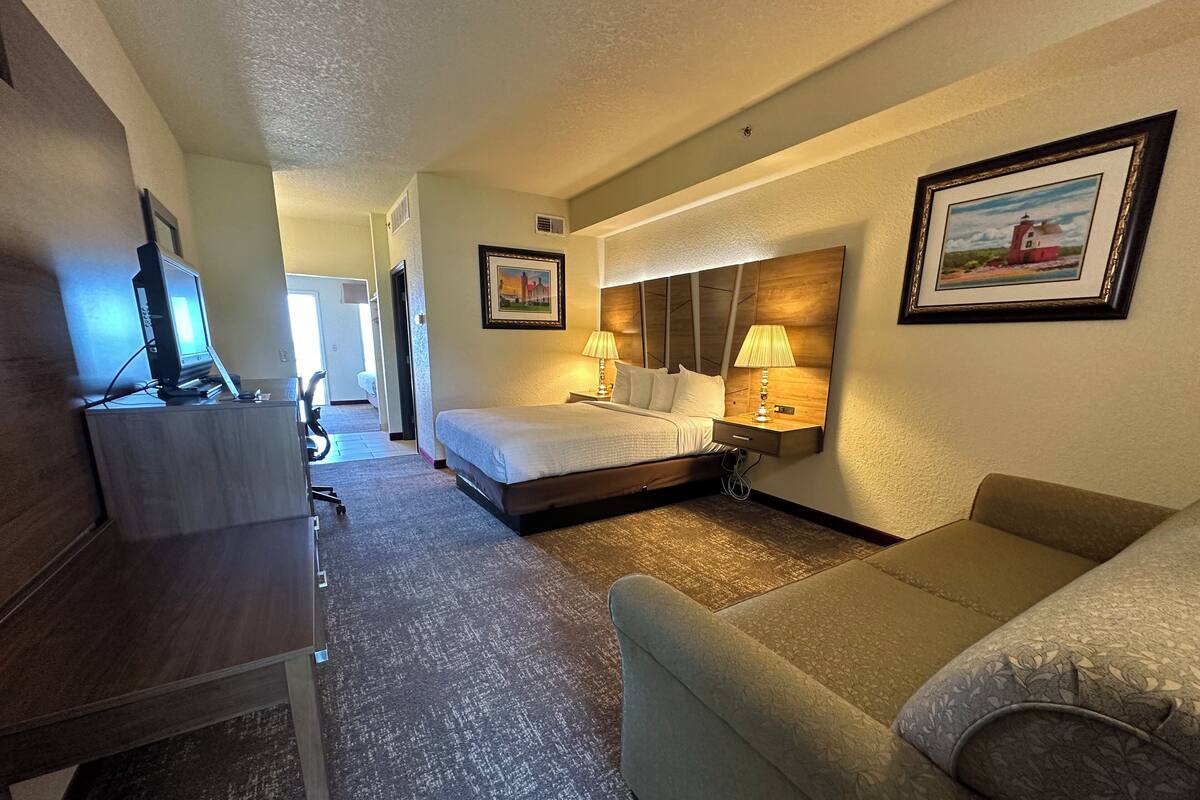 Ein Hotelzimmer mit einem Bett, einem Schreibtisch mit Computer, einer Couch und einem Bild an der Wand.