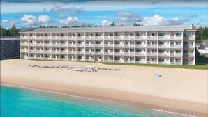 A multi-story hotel with balconies, located on a beach with clear turquoise waters.