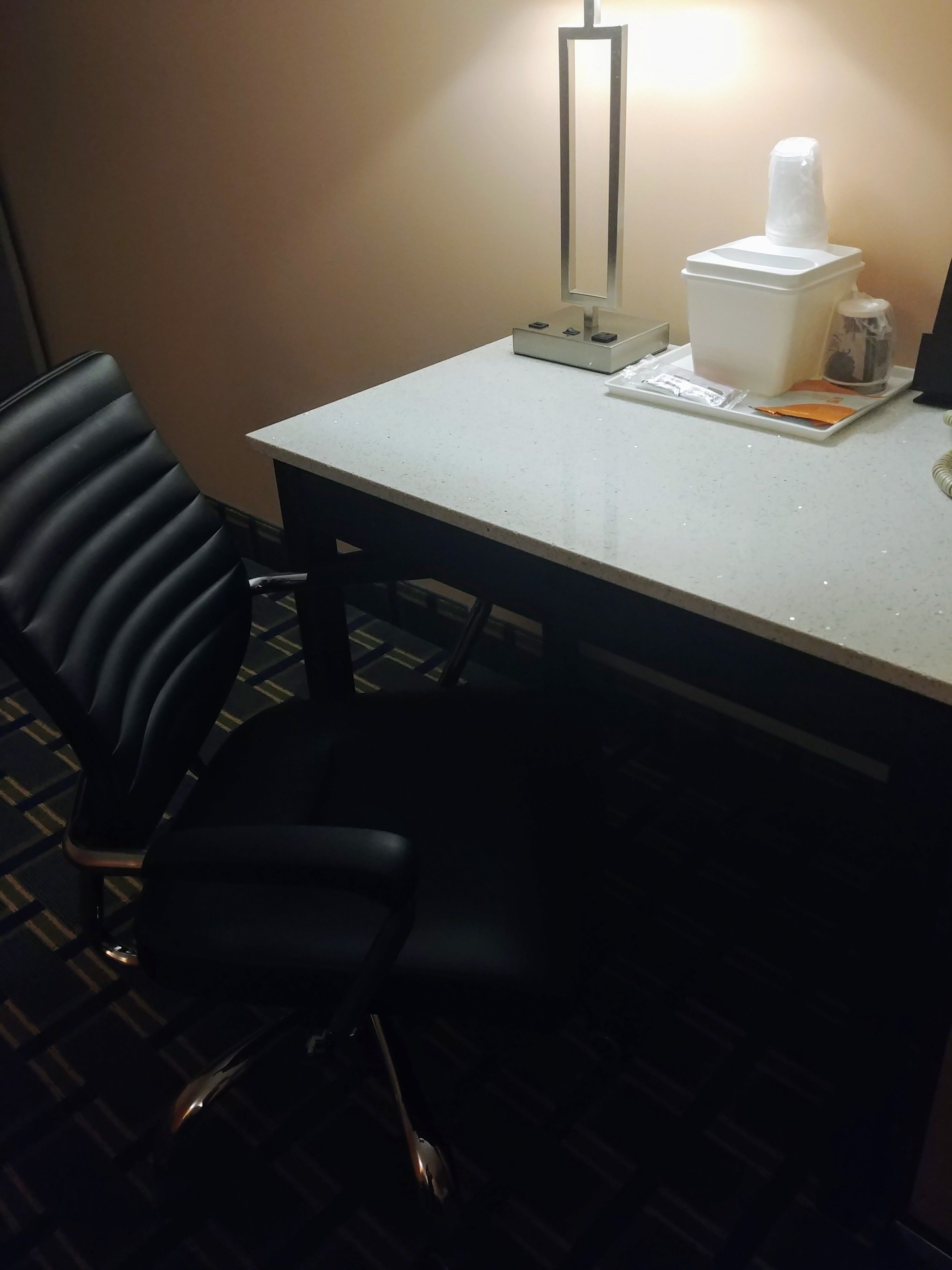 A hotel room with a white table, black chairs, a mirror, a tissue box, and a small bottle.