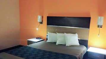 Una habitación de hotel con cama, mesitas de noche y lámparas de pared.