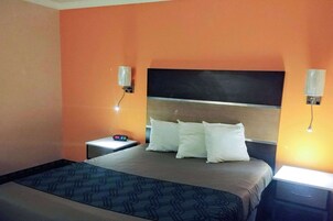 Una habitación de hotel con cama, mesitas de noche y lámparas de pared.