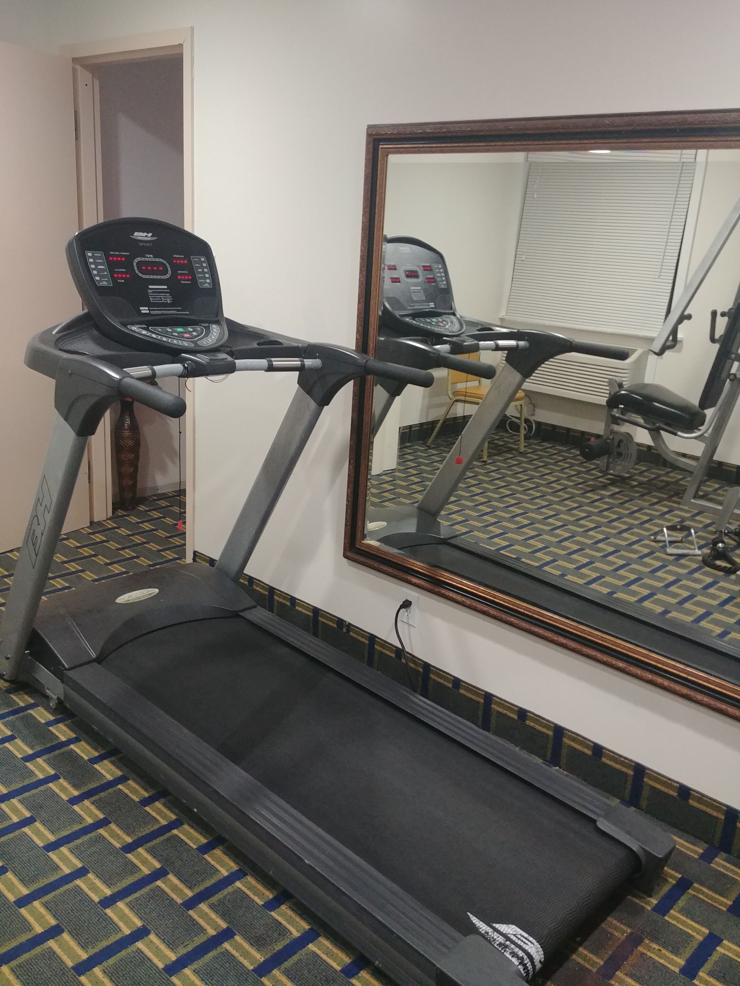 Una cinta de correr en una habitación de hotel, con un espejo que refleja el espacio.