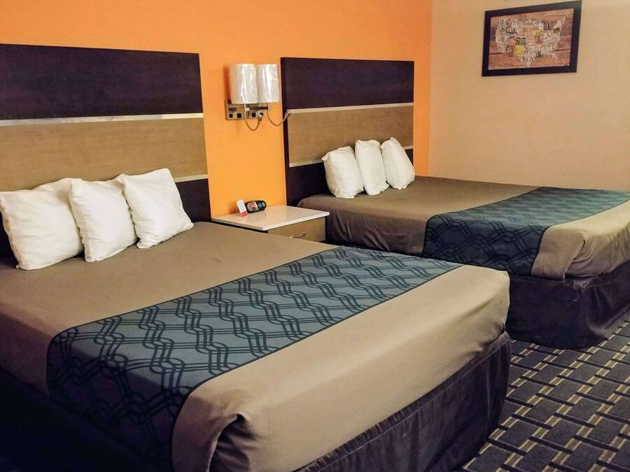 Habitación de hotel con dos camas, cada una con cabecera, una mesita y una lámpara de pared.