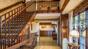 Un hall d’hôtel avec un escalier en bois, un comptoir d’accueil et une vue dégagée sur l’extérieur grâce à de grandes fenêtres.