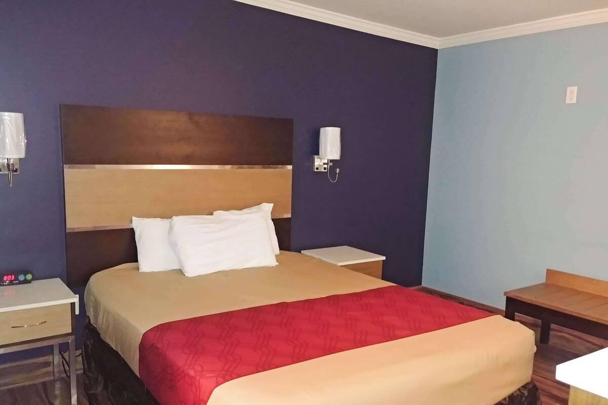 Une chambre d’hôtel avec un grand lit, une table de chevet, une commode, un téléphone fixé au mur et une petite table.