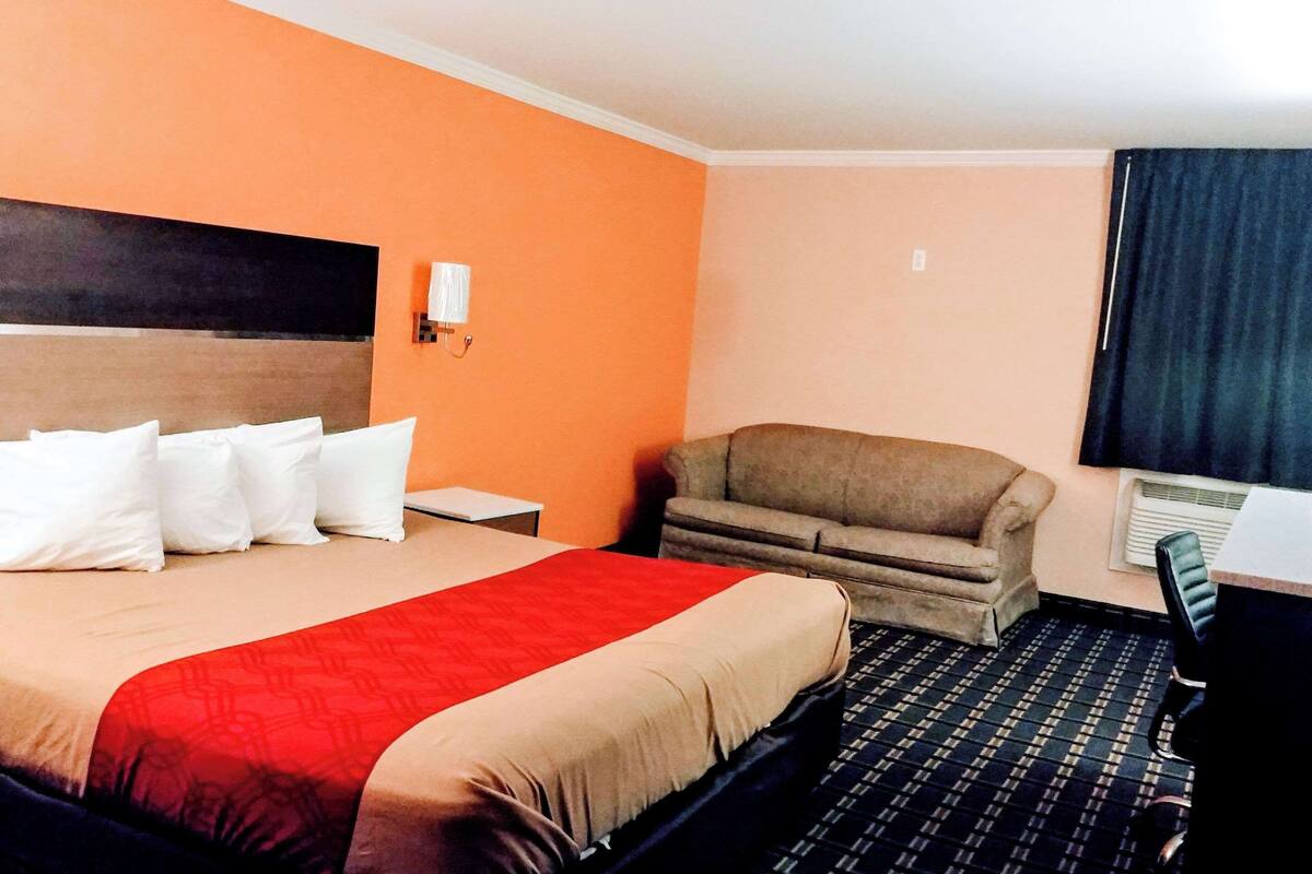 Une chambre d’hôtel avec un grand lit, un canapé, un bureau et une fenêtre avec des rideaux.