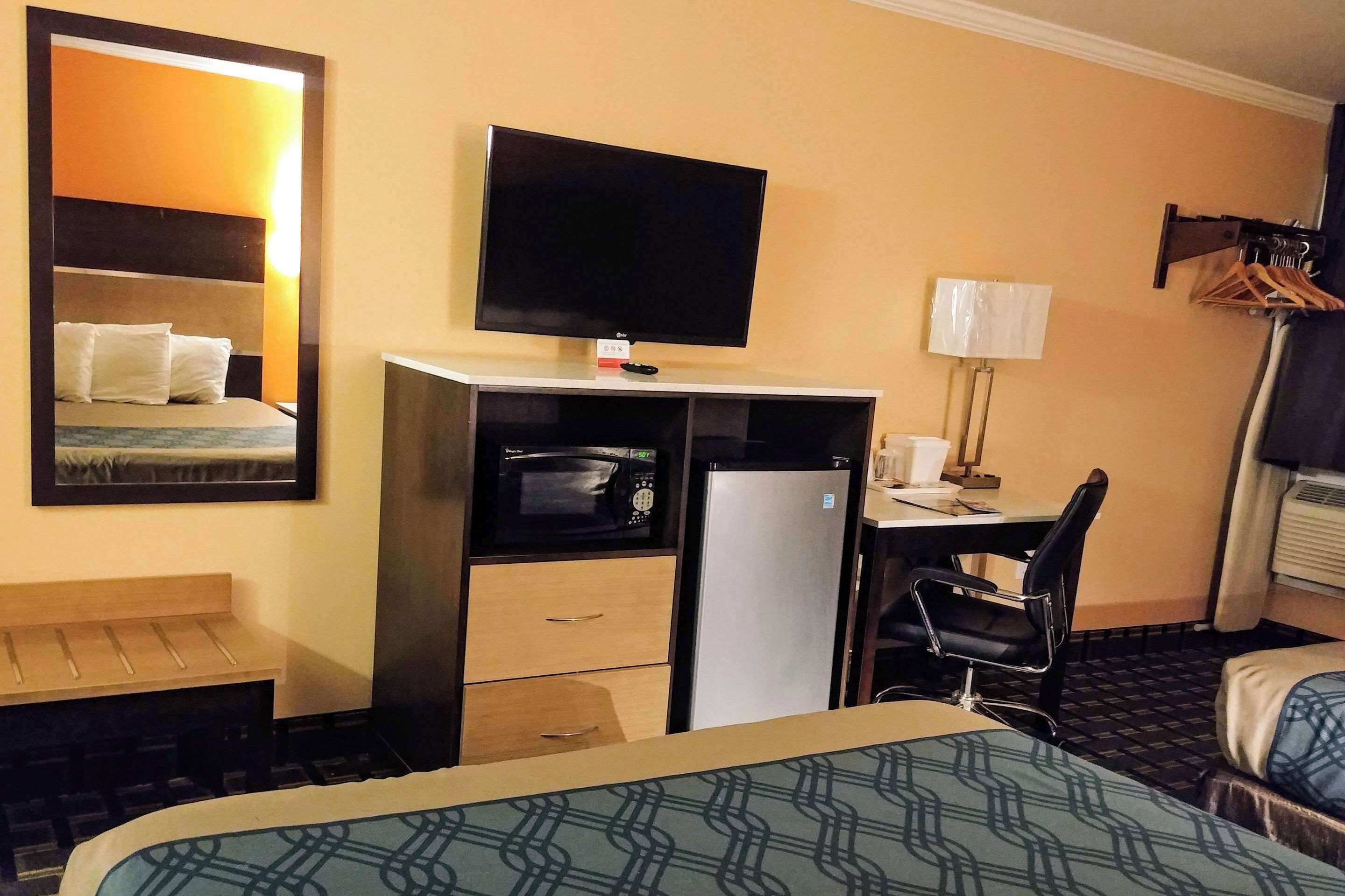 A hotel room with a bed, a desk with a chair, a television, a microwave, a refrigerator, and a mirror.