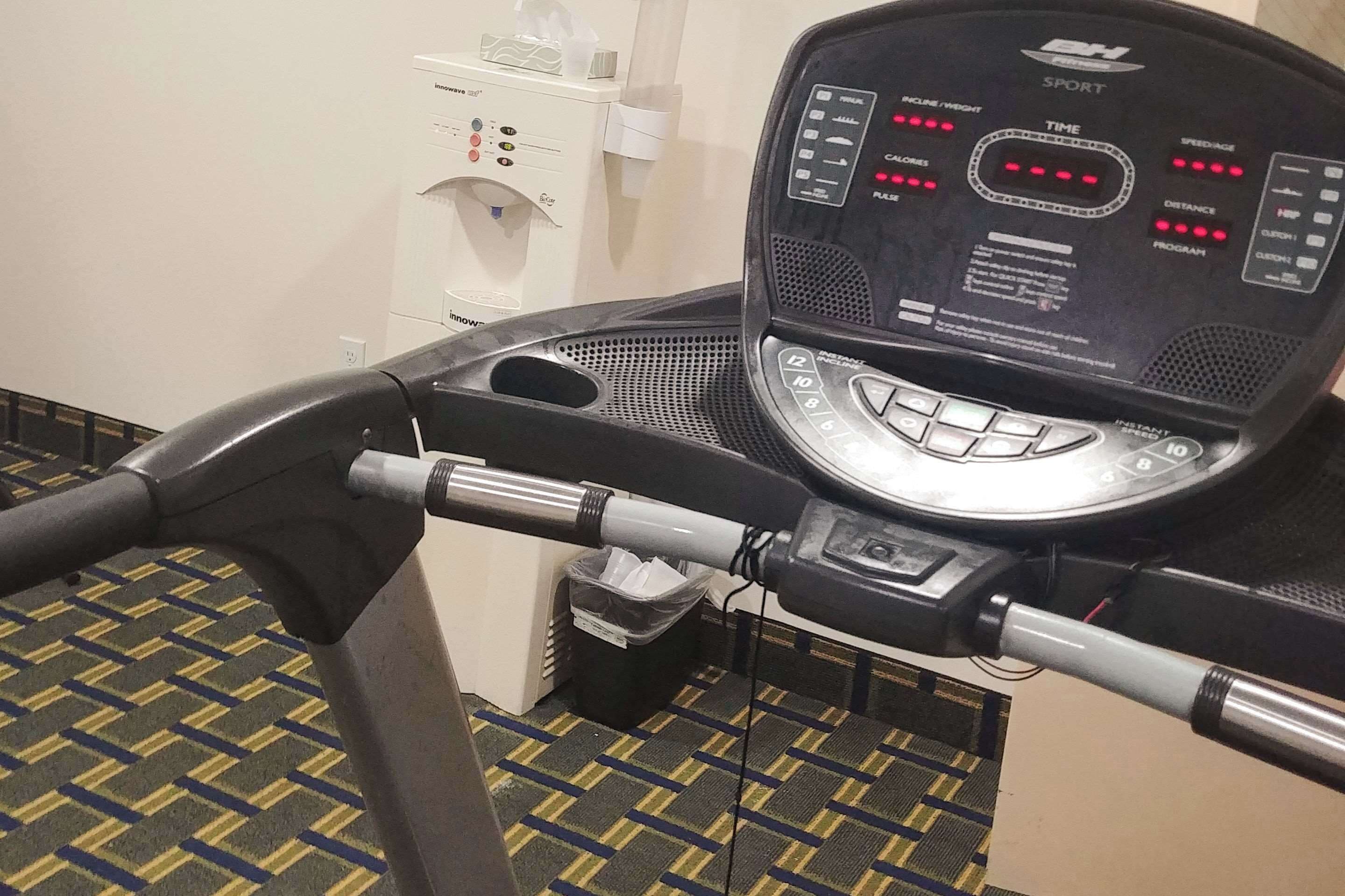 Una bicicleta estática con pantalla digital, dispensador de agua y cubo de basura.