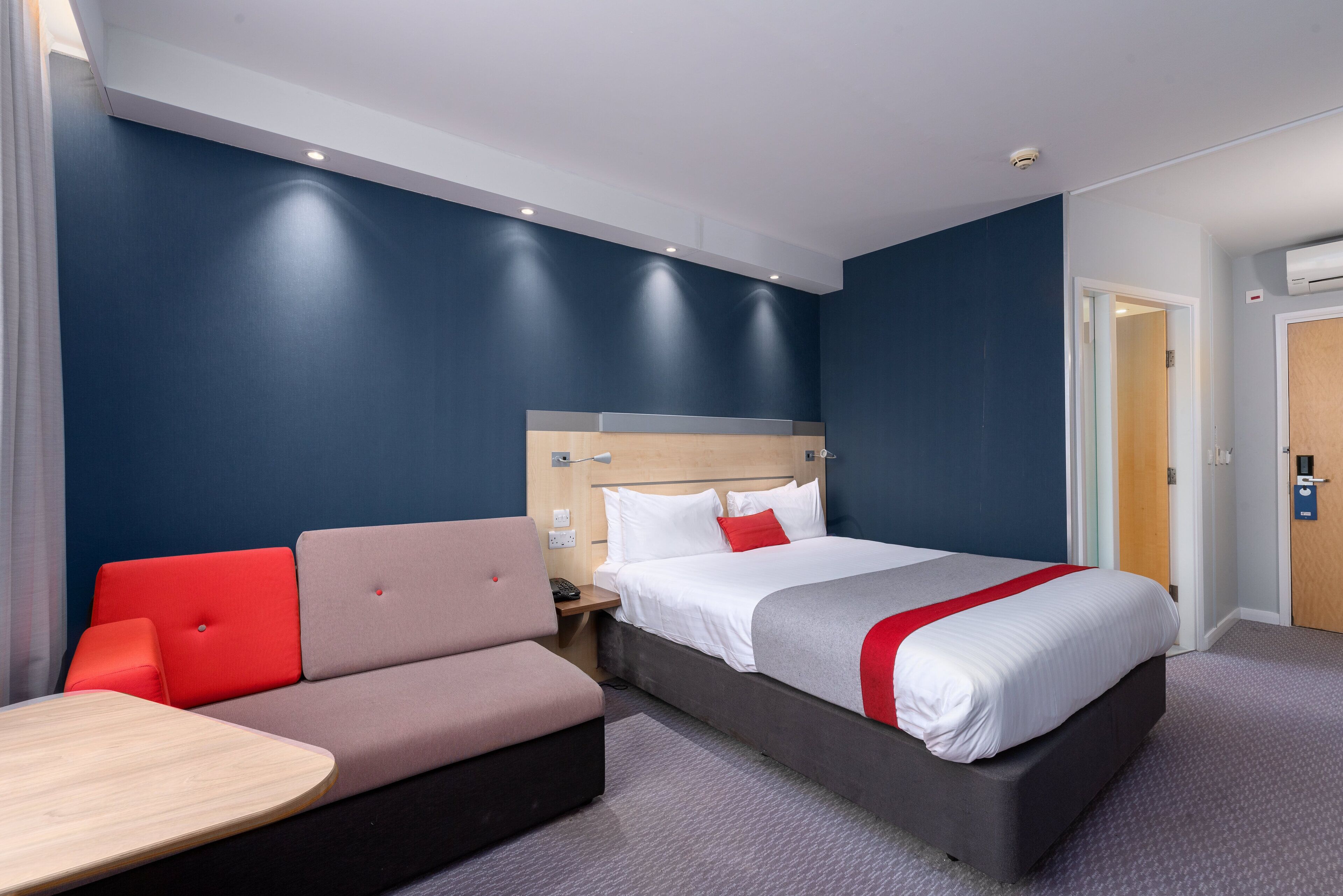 A hotel room with a bed, a sofa, a small table, and a nightstand.