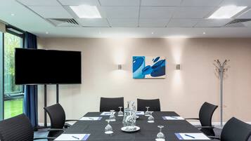 Un salón de conferencias con una mesa grande, sillas, un televisor de pantalla plana y un cuadro en la pared.