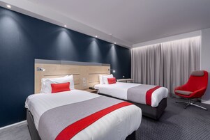 Habitación de hotel con dos camas, una silla roja y un ventanal con cortinas.