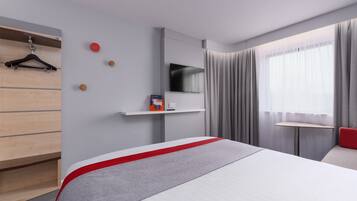 A modern hotel room with a bed, a TV mounted on the wall, a small table, and a red chair.
