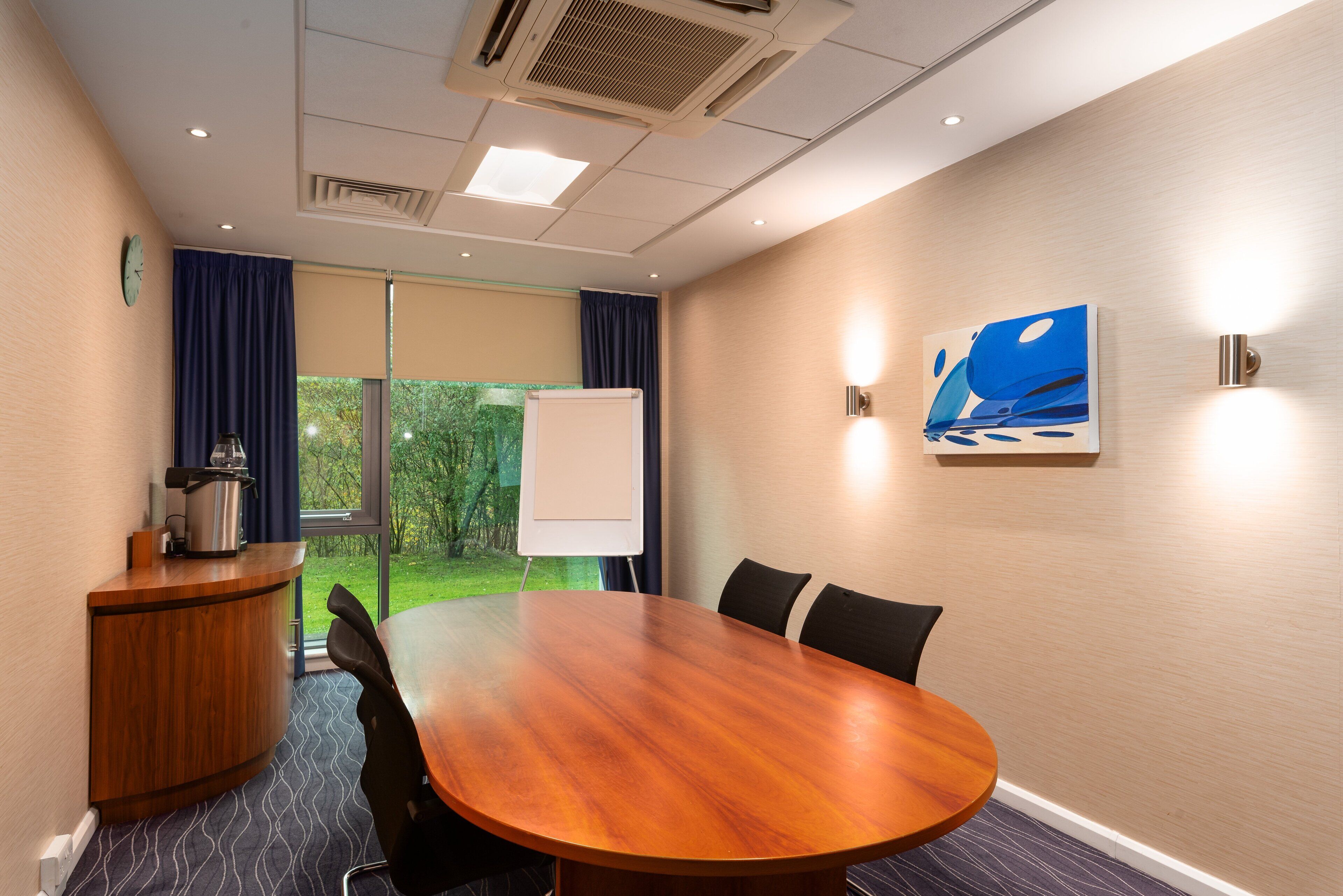 A conference room with a wooden table, chairs, a whiteboard, and a view of greenery outside.