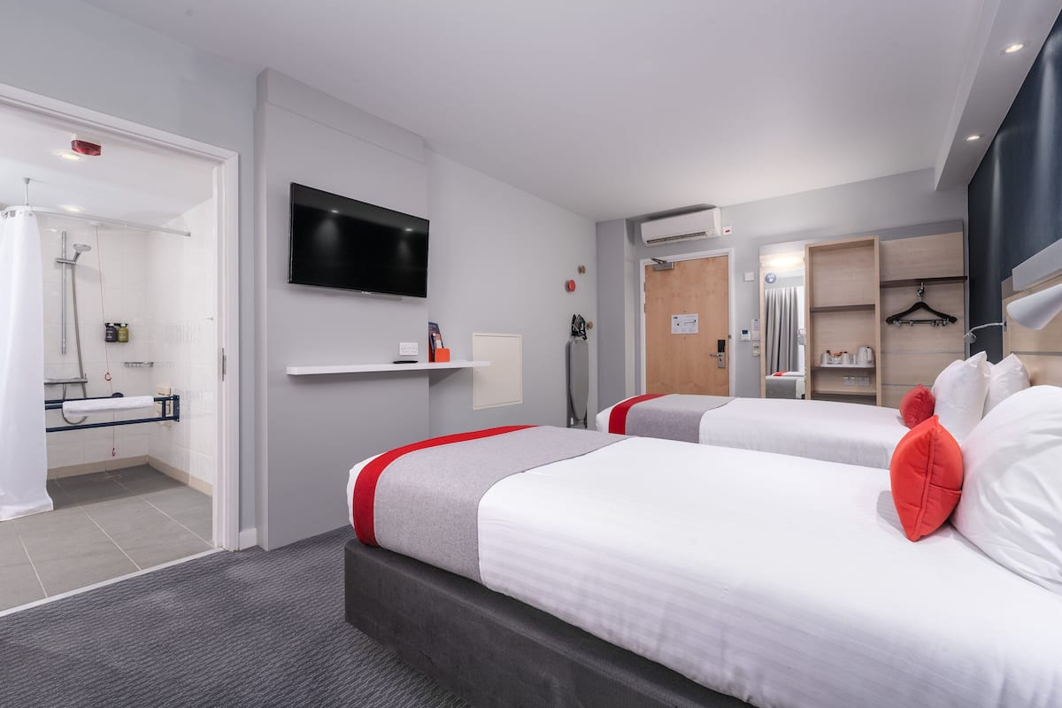 A hotel room with two beds, a TV, a shower, and a small bathroom.