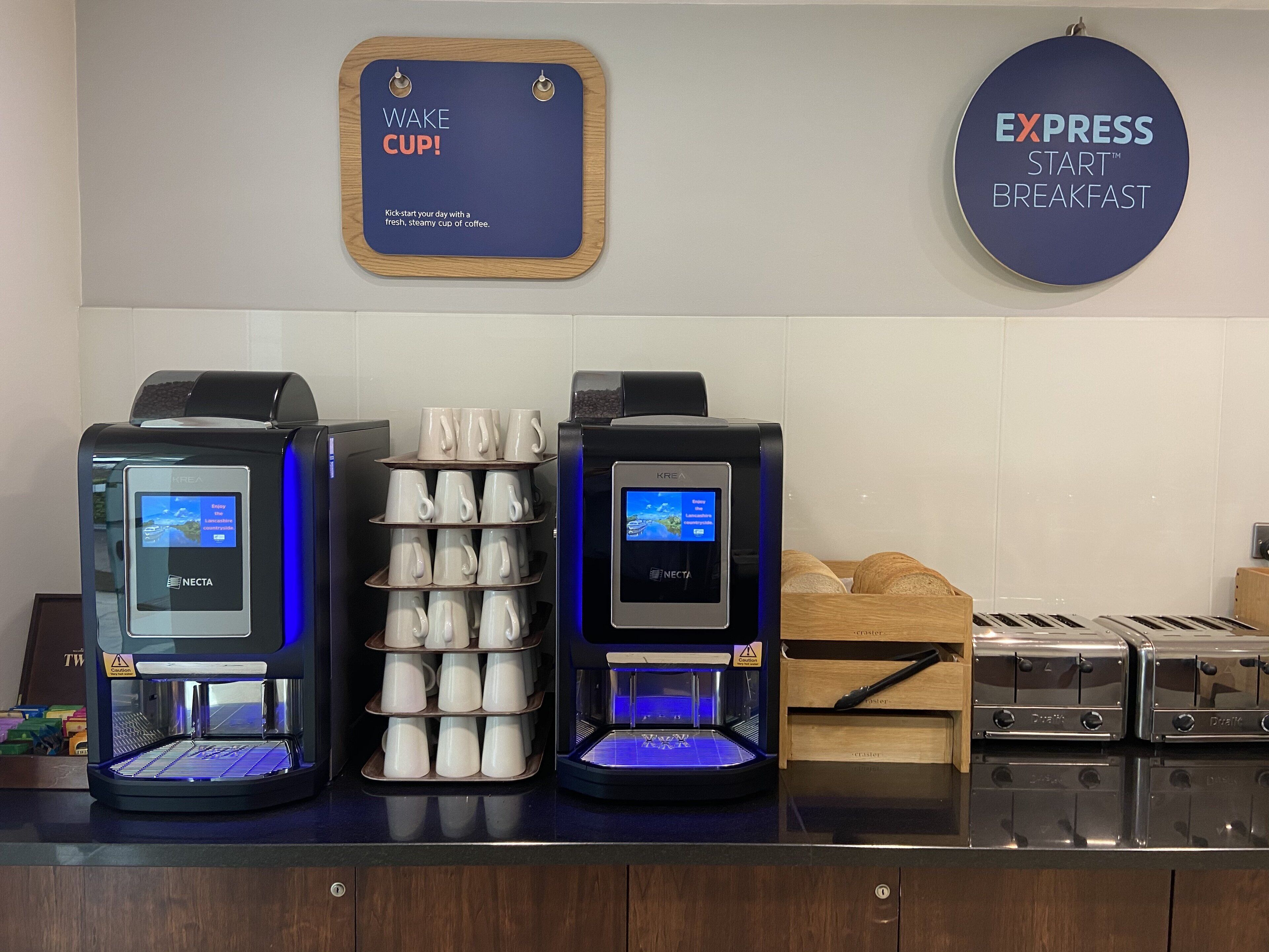 Una estación de café con dos máquinas de café y una pila de vasos desechables.