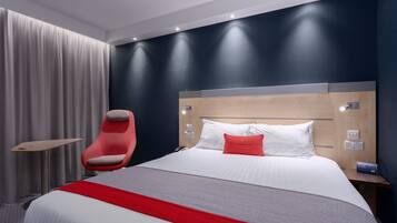 A modern hotel room with a large bed, a red chair, a bedside table, and a nightstand.