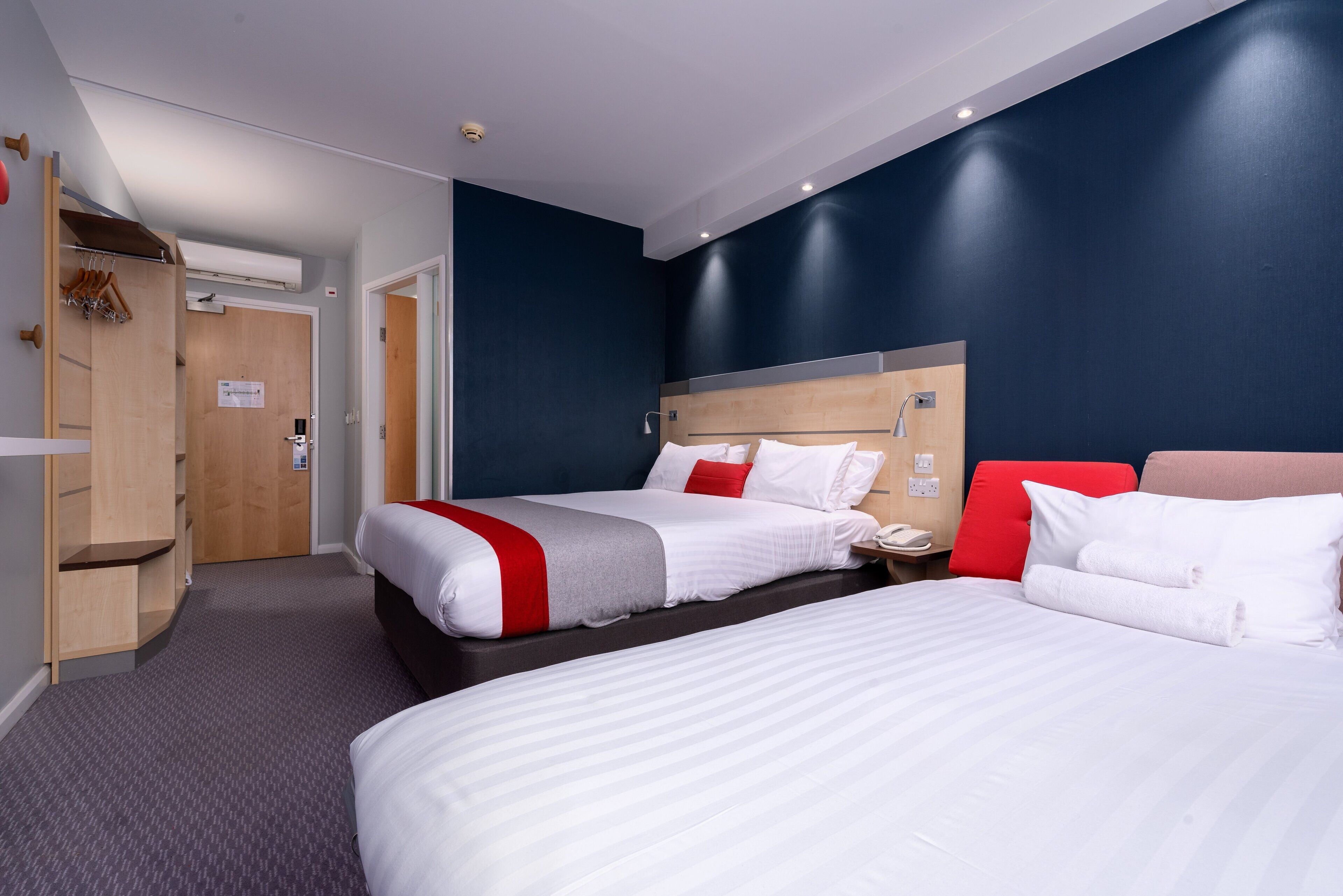 Een hotelkamer met twee bedden, een houten garderobe, een bureau en een nachtkastje.