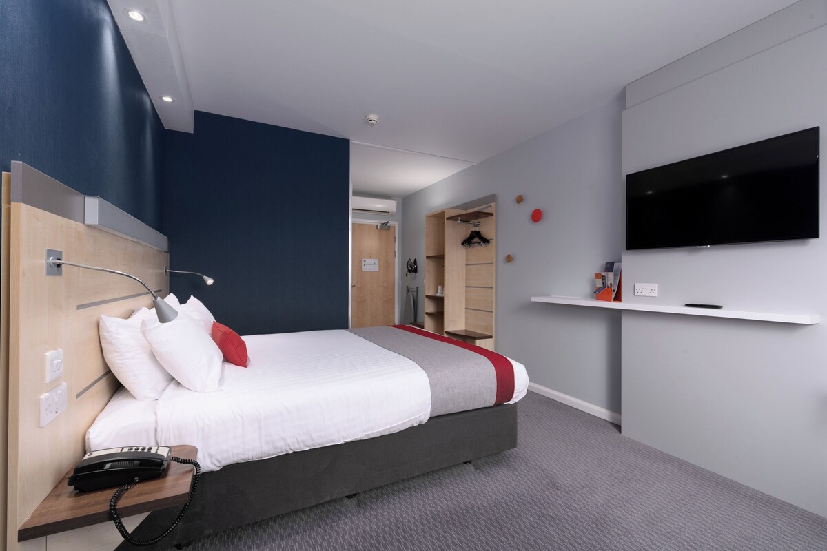A modern hotel room with a large bed, bedside telephone, and a mounted television.