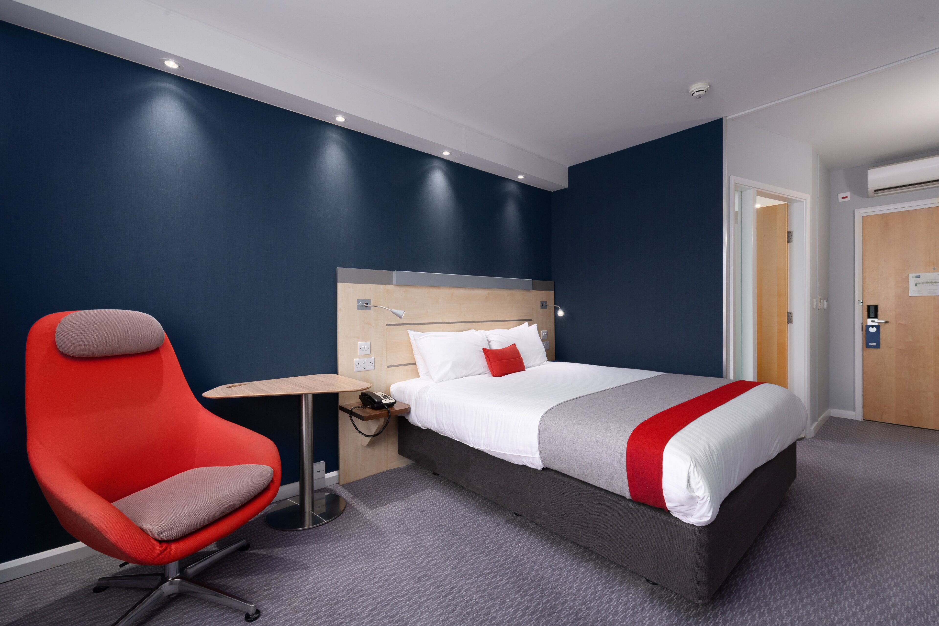 Une chambre d’hôtel avec un lit, une chaise rouge, une petite table et une table de chevet.