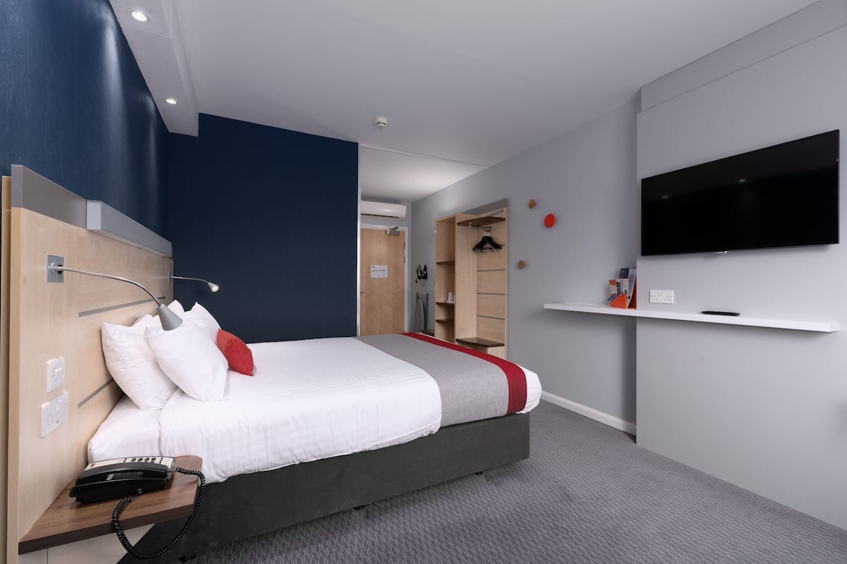 A modern hotel room with a large bed, bedside telephone, and a mounted television.