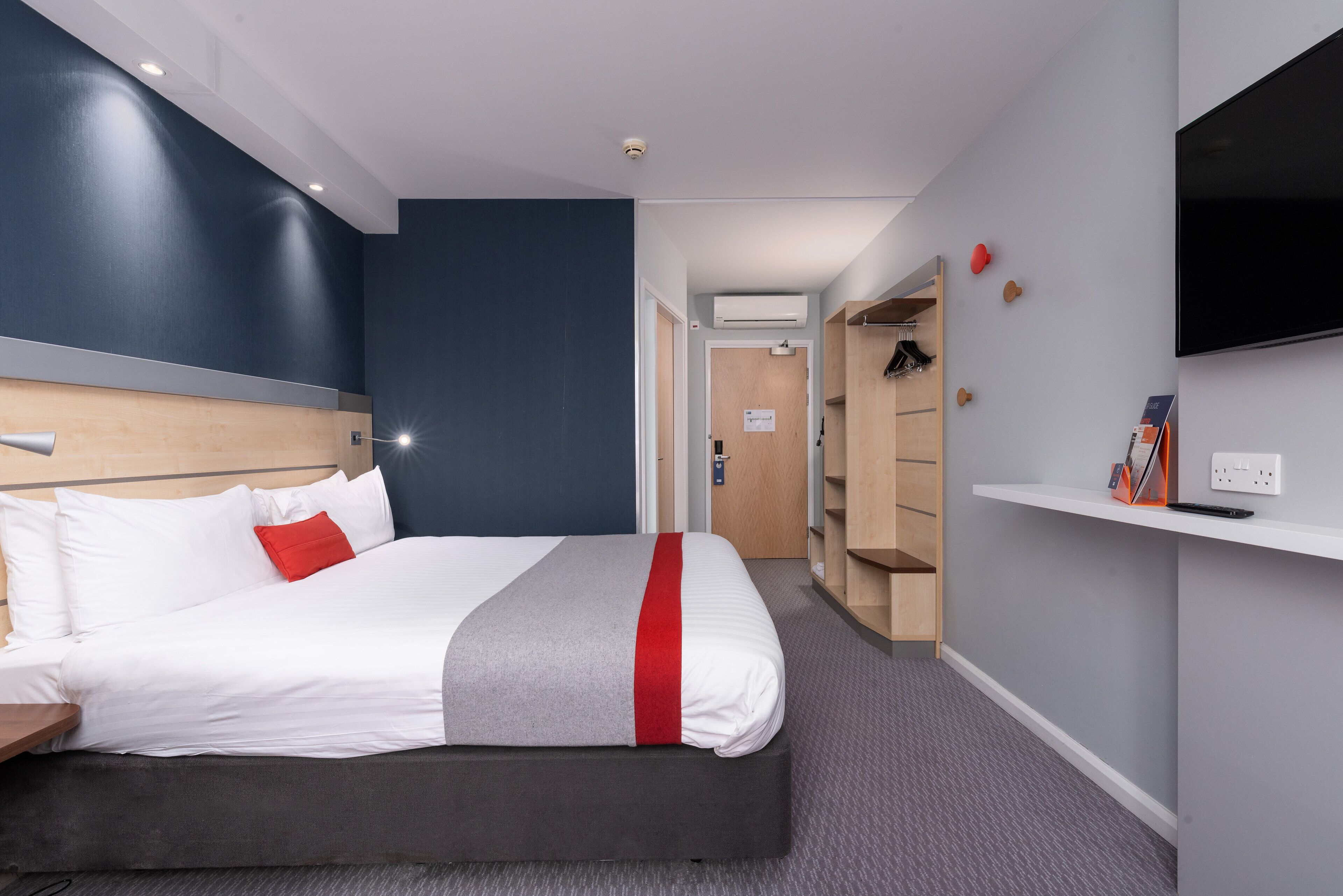 A modern hotel room with a large bed, a TV mounted on the wall, and a walk-in closet.