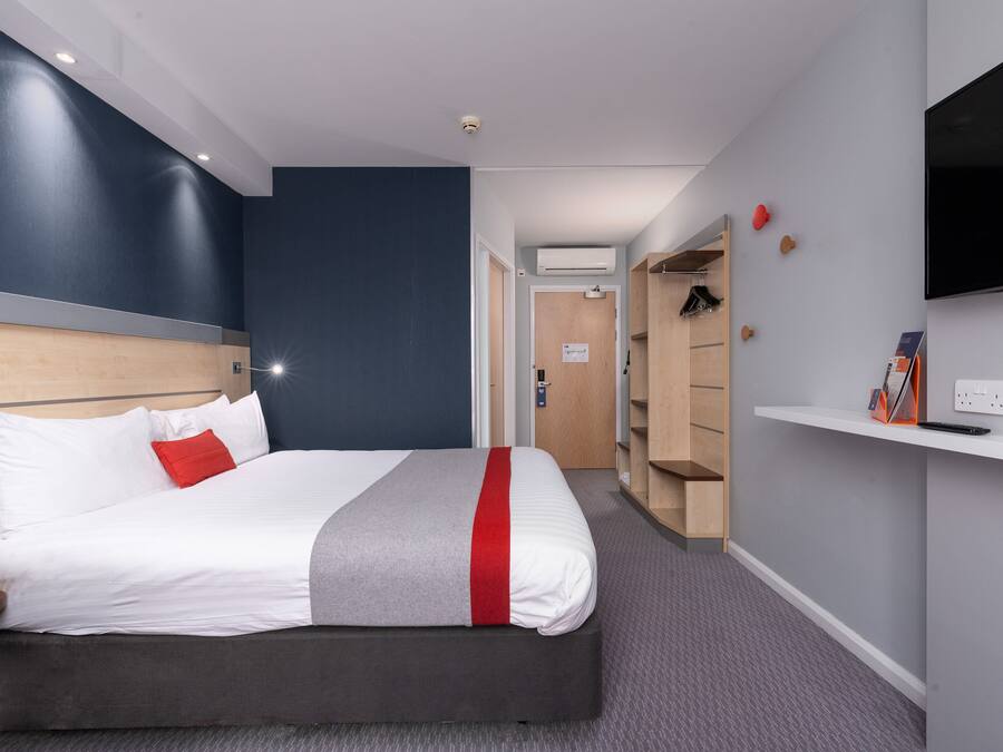 A modern hotel room with a large bed, a TV mounted on the wall, and a walk-in closet.