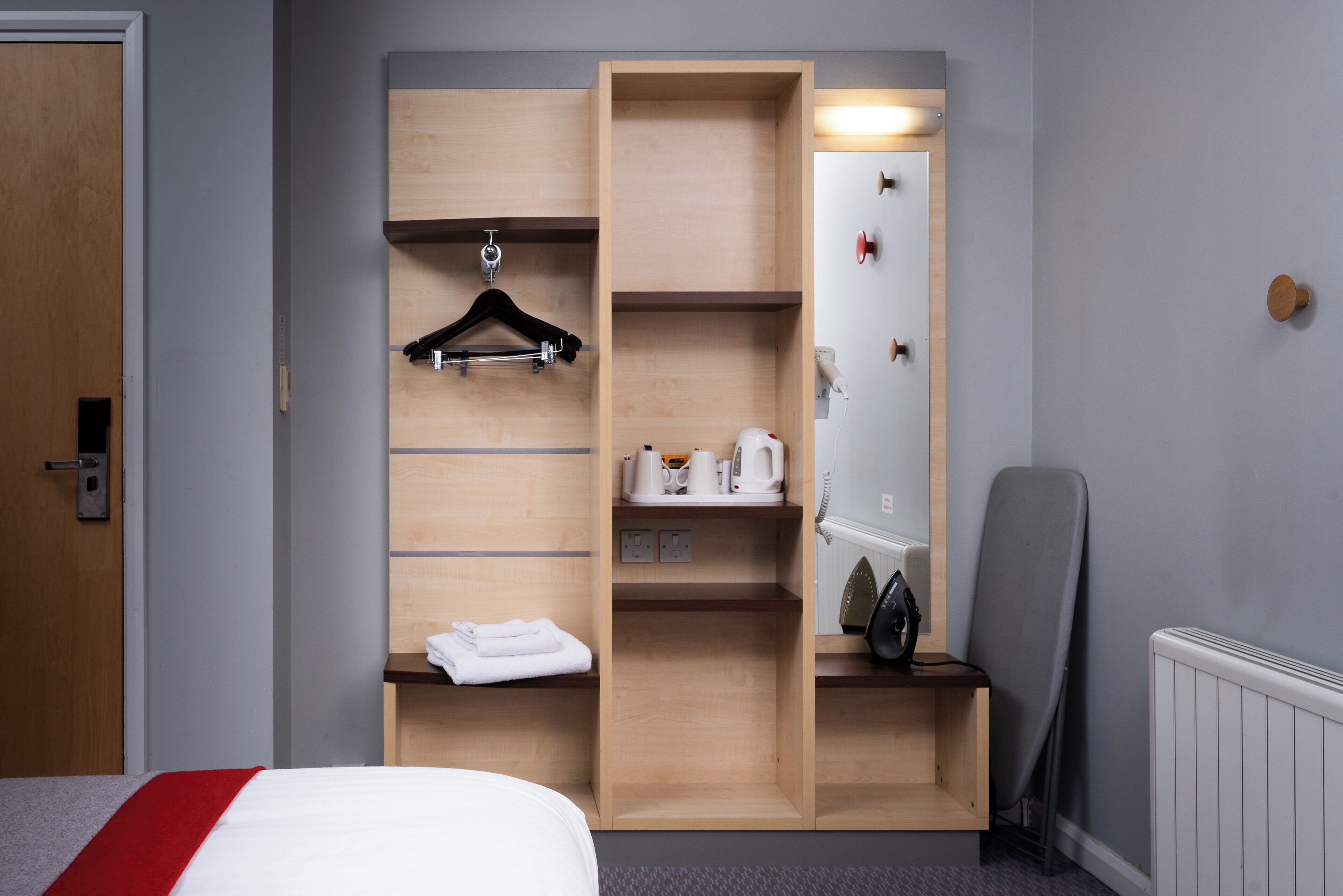 A hotel room with a bed, a wooden wardrobe with a mirror, a hairdryer, and a radiator.
