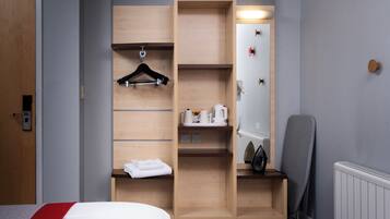A hotel room with a bed, a wooden wardrobe with a mirror, a hairdryer, and a radiator.