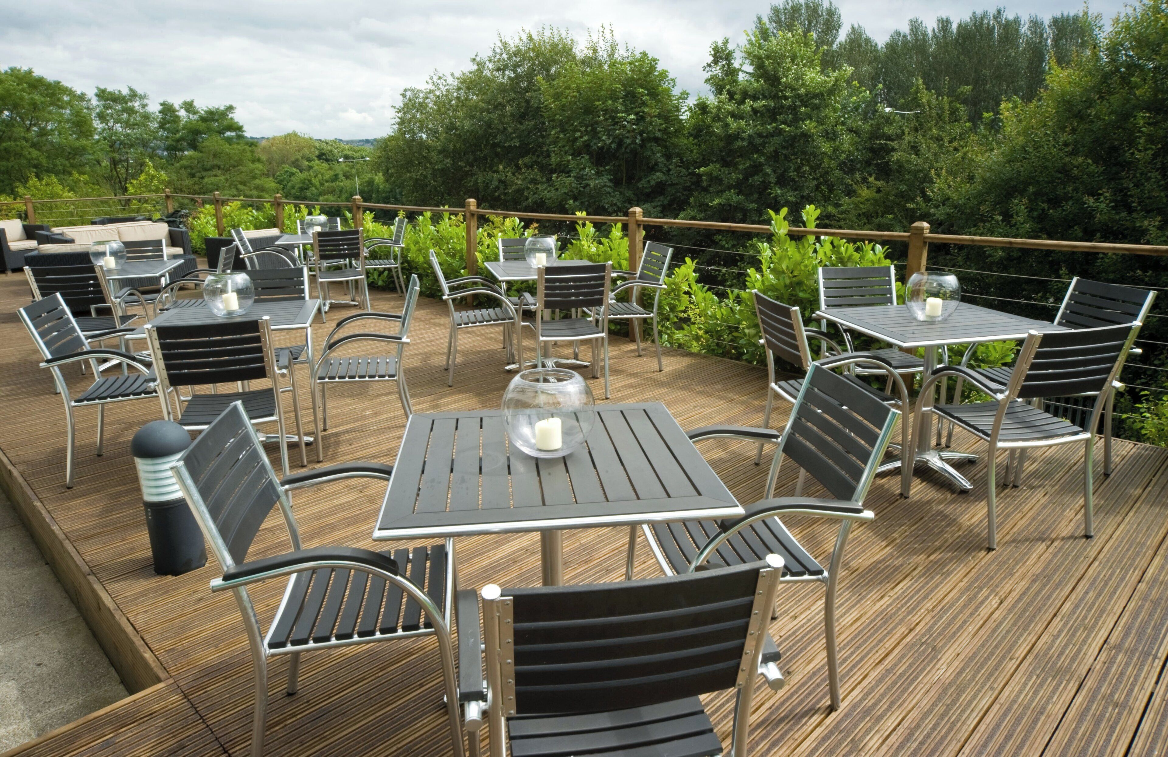 An outdoor patio with multiple tables and chairs, surrounded by greenery.