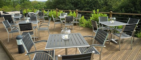Un patio al aire libre con varias mesas y sillas, rodeado de follaje.