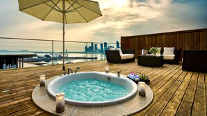 A wooden deck with a hot tub, lounge chairs, and an umbrella.