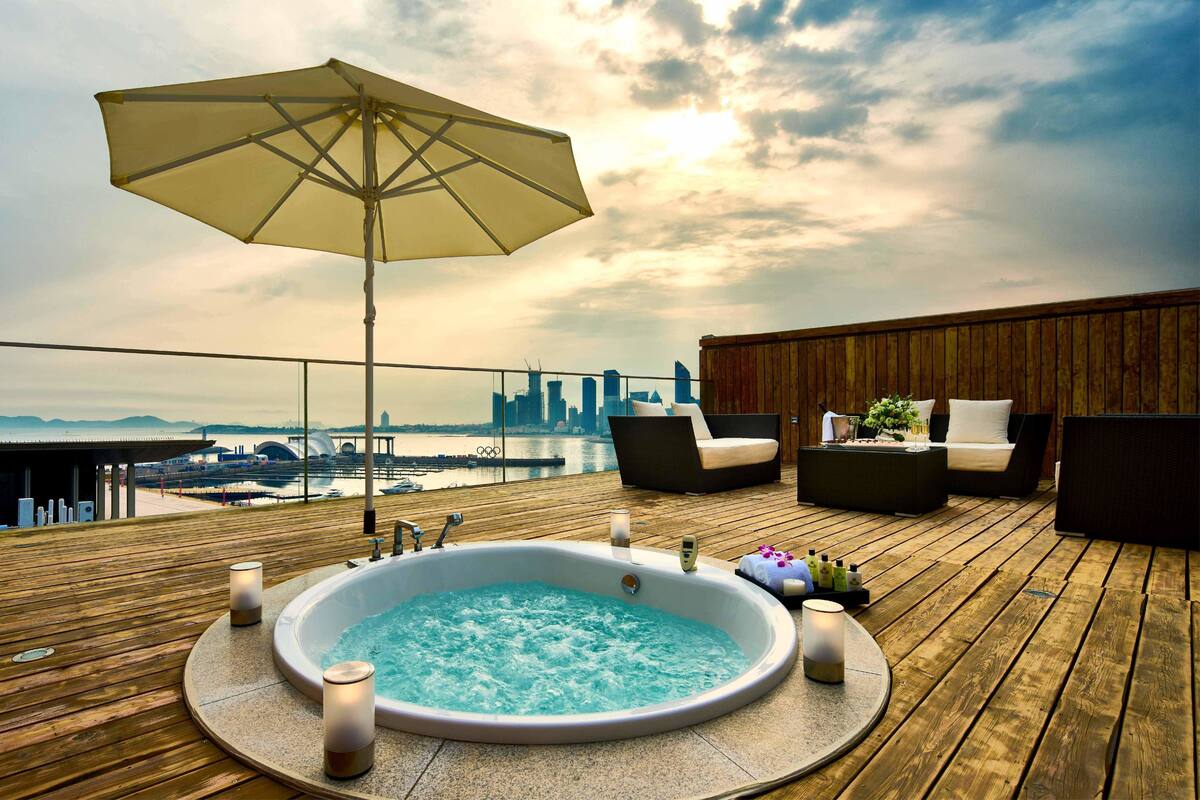 A wooden deck with a hot tub, lounge chairs, and an umbrella.