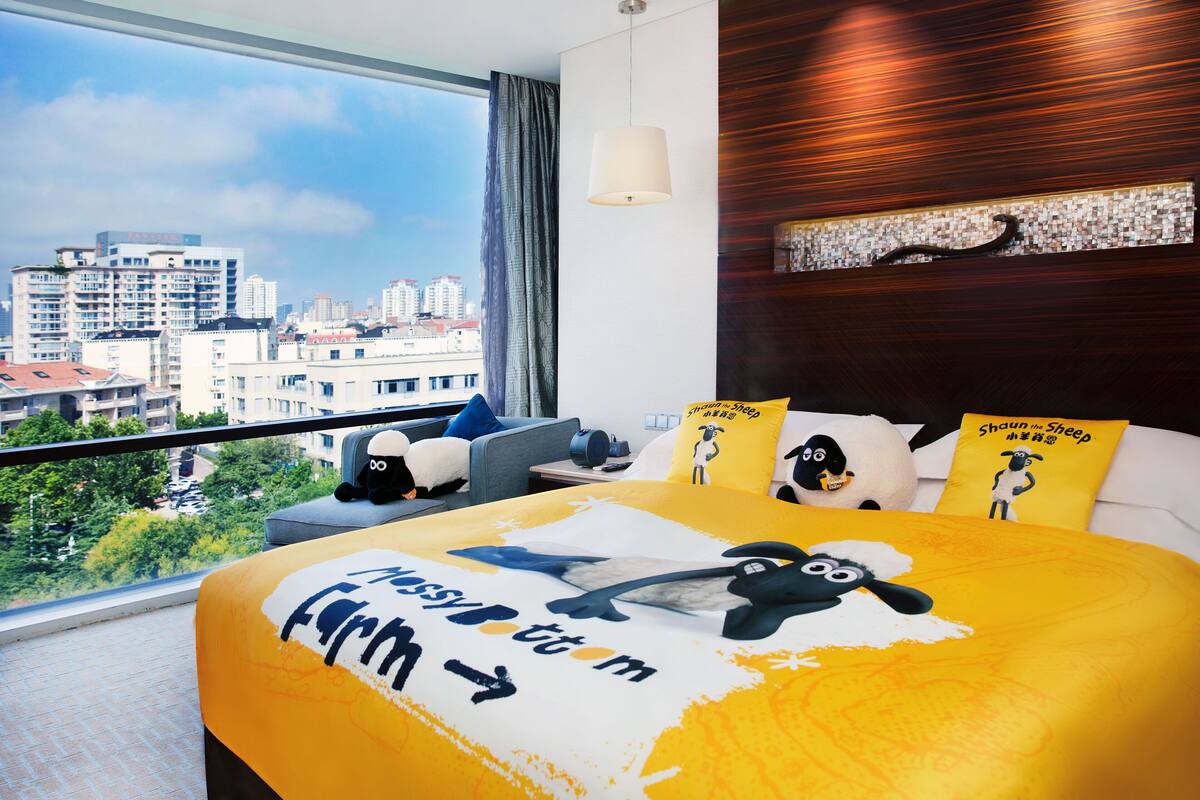 A modern hotel room with a large bed, city view, and a decorative wall.