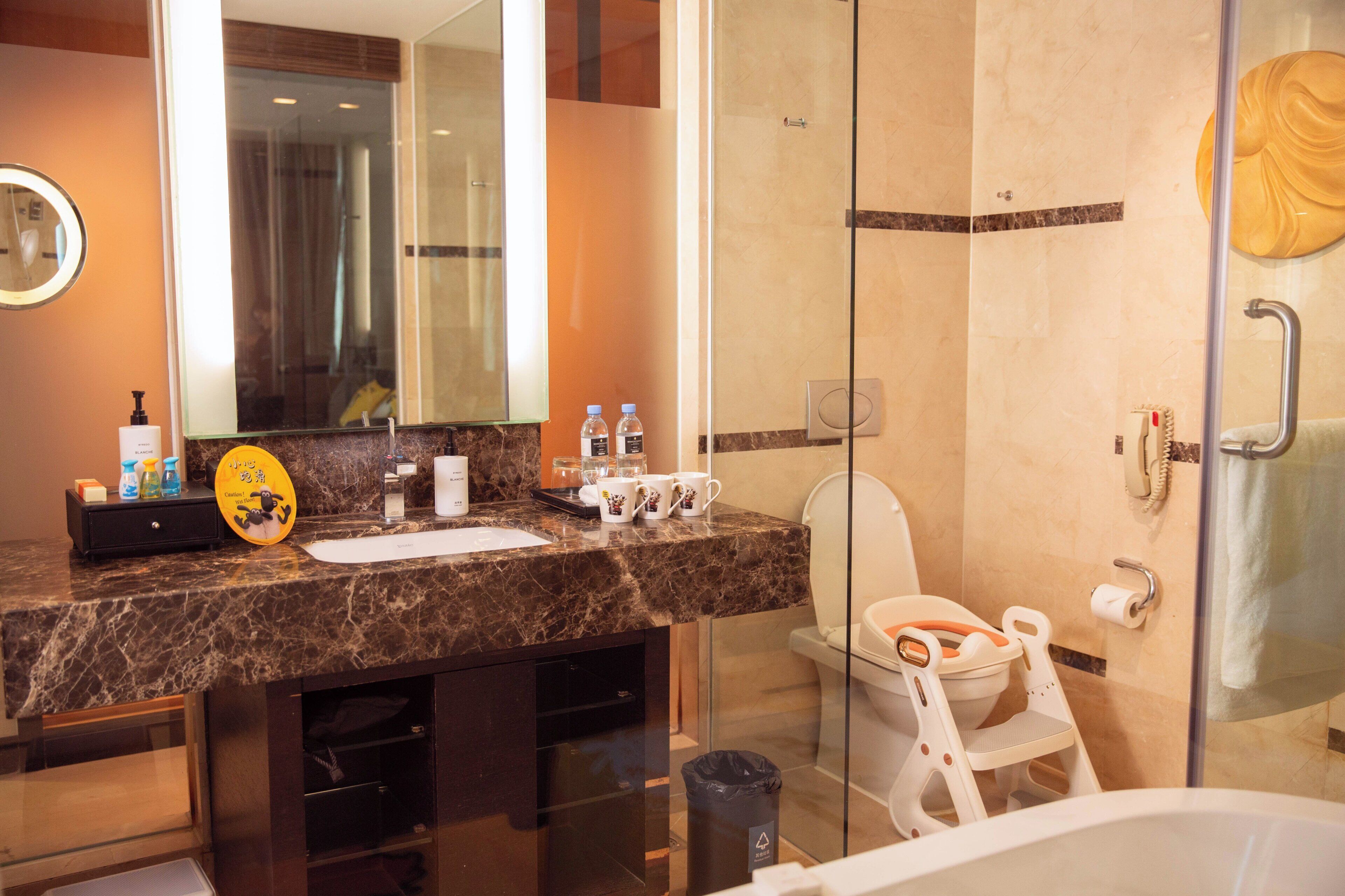 A modern bathroom with a marble countertop, a glass shower enclosure, a toilet with a child seat, and a large mirror.