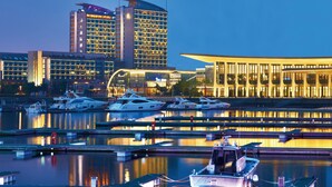 A marina with several yachts docked, a modern building with a curved facade, and a high-rise hotel with illuminated windows. - InterContinental Qingdao by IHG (Qingdao)