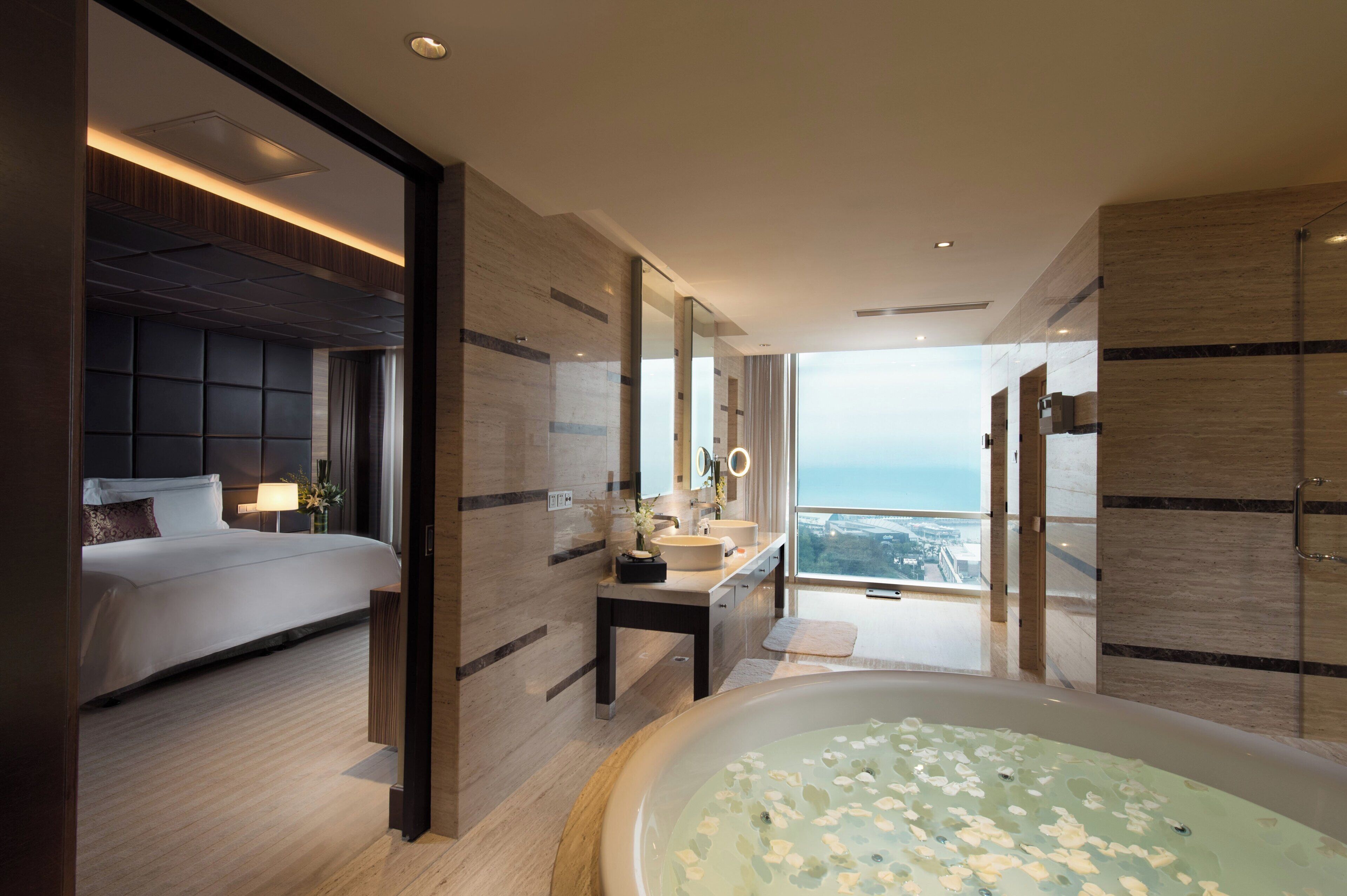 A modern hotel room with a large bed, a bathroom with a bathtub, and a view of the city.