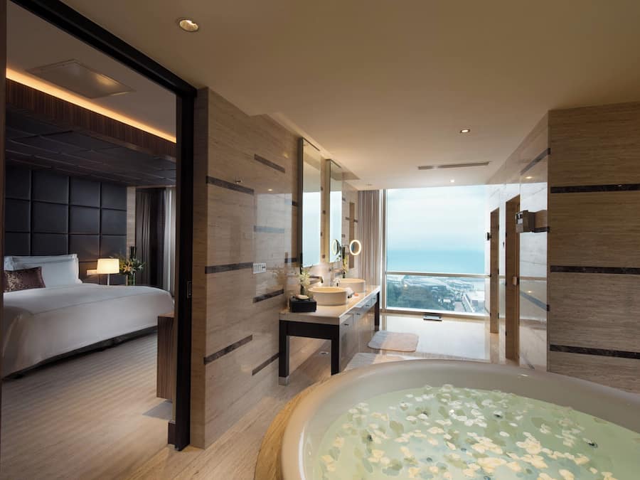 Una habitación de hotel moderna con una cama grande, un baño con bañera y vistas a la ciudad.