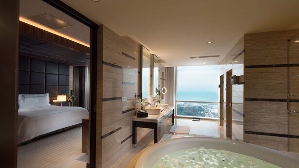 A modern hotel room with a large bed, a bathroom with a bathtub, and a view of the city.