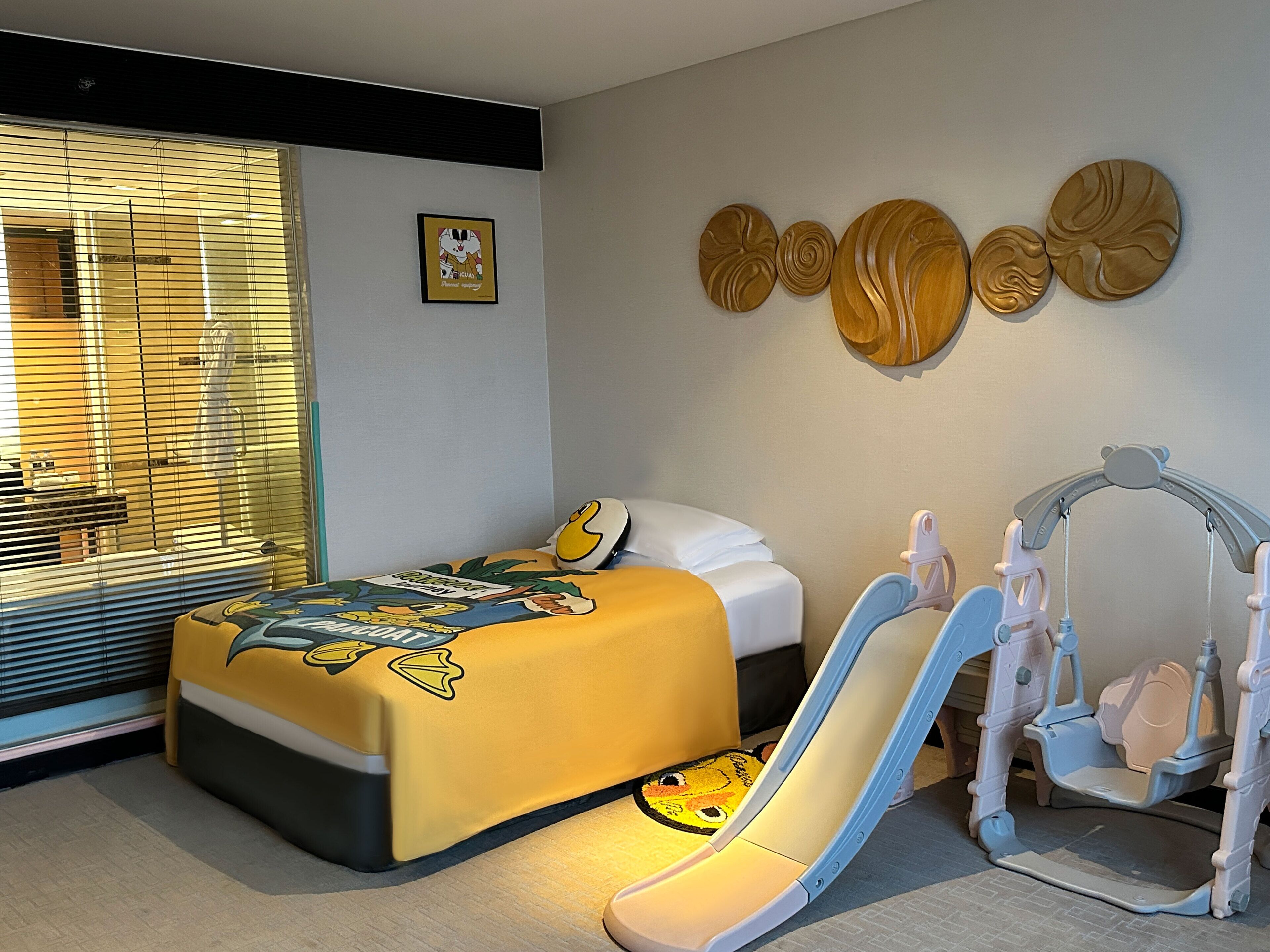 Un dormitorio con cama, ventana con persianas, un cuadro colgado en la pared y una zona de juegos infantiles.