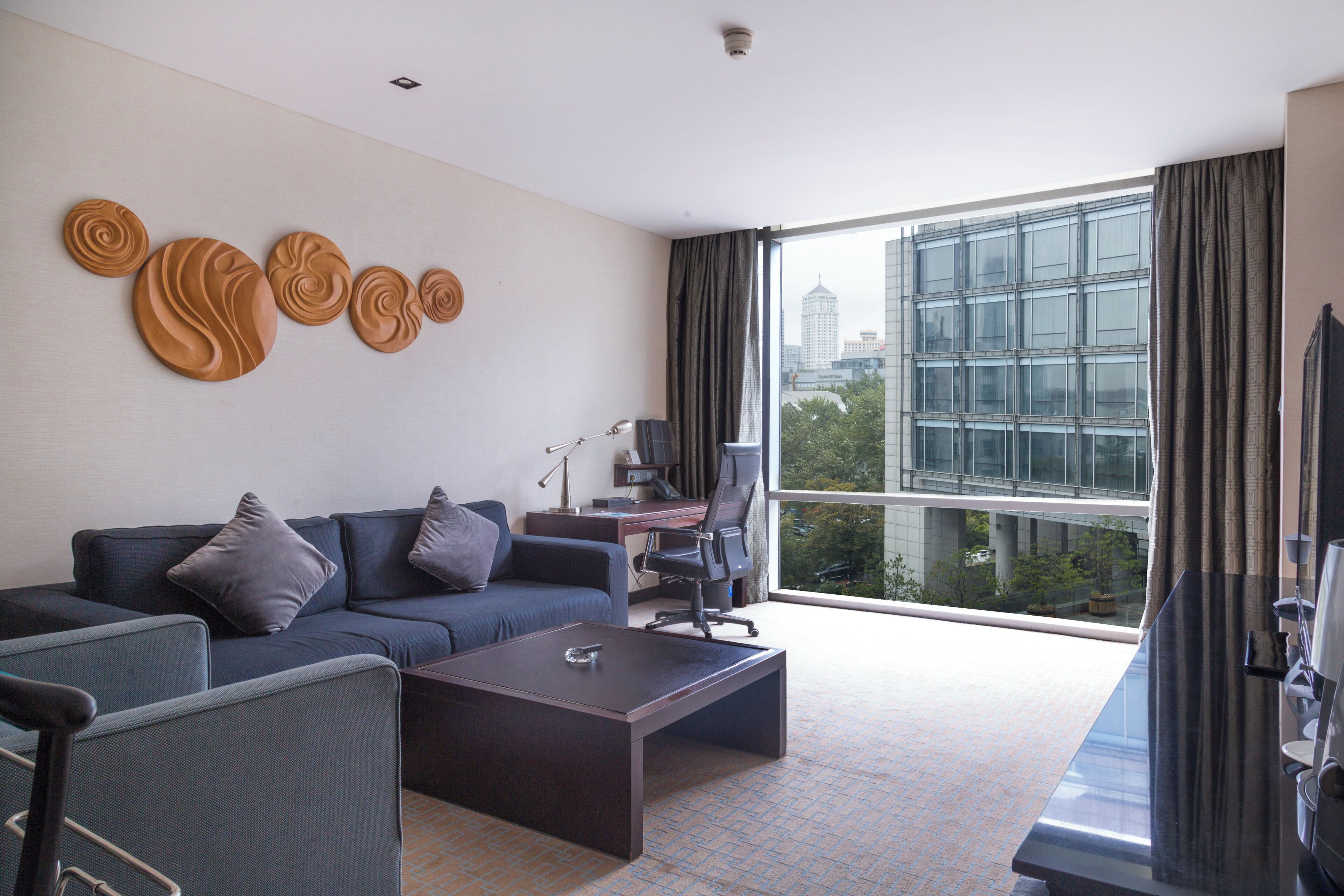 Ein modernes Hotelzimmer mit großem Fenster, einer Couch, einem Schreibtisch und einem Sessel.