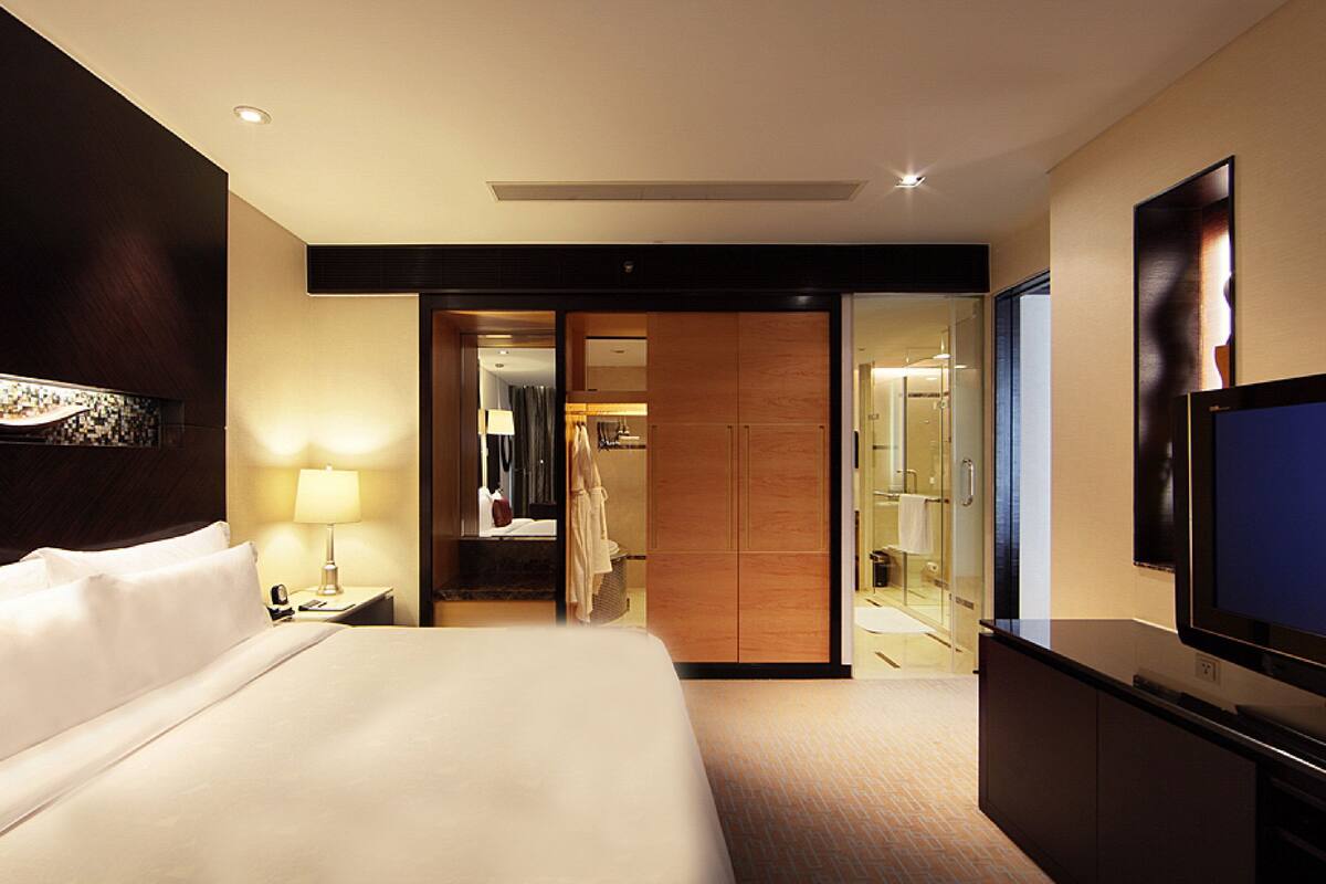 A hotel room with a large bed, a TV, a bathroom with a glass shower, and a walk-in closet.