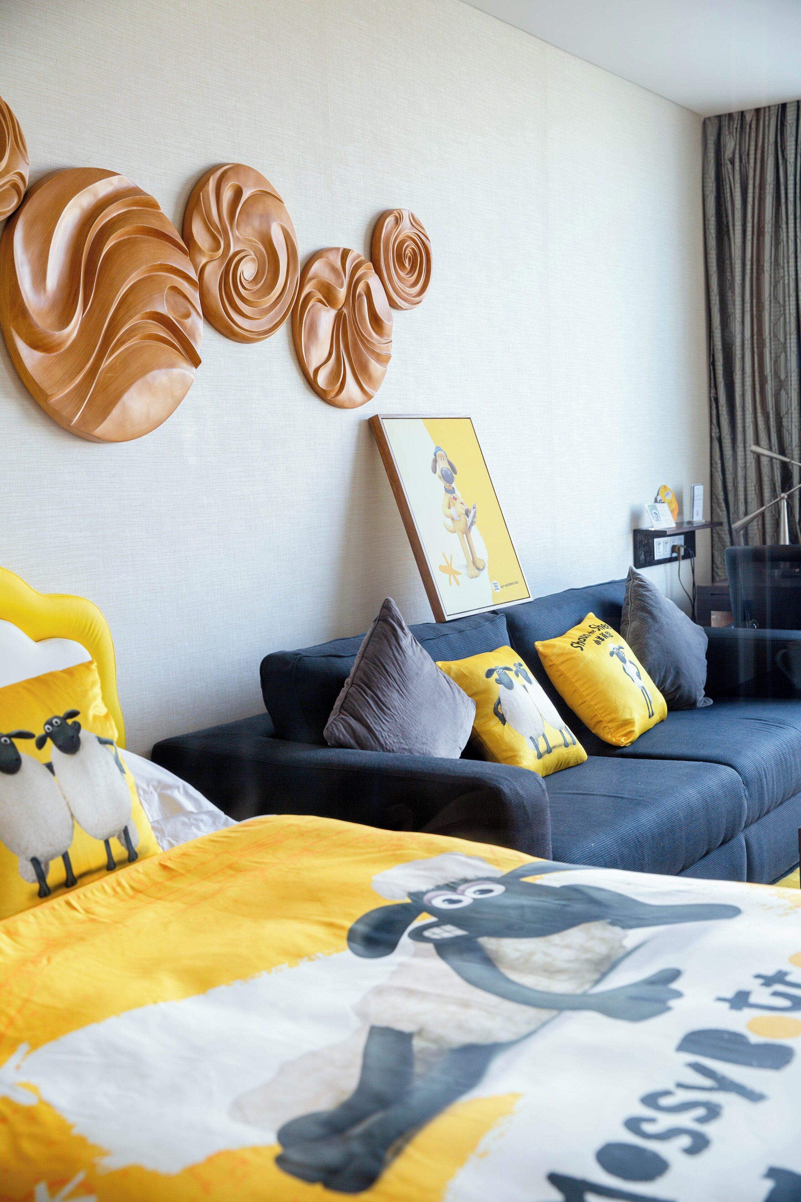 A modern living room with a sofa, yellow and gray pillows, a bed with a yellow and white comforter, and wall decor.