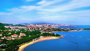 A coastal cityscape with a prominent urban area, a beach, and a clear view of the sea.